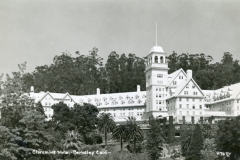Black and white photo of the Claremont Hotel in Berkeley, California, surrounded by trees. The grand building has a multi-windowed facade, steep roofs, and a central tower with a flagpole, set against a backdrop of tall trees.