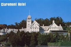 View of the historic Claremont Hotel, a grand white building with a central tower, surrounded by lush greenery and set against a clear blue sky.