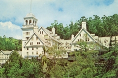 A large, historic white building with a tower surrounded by lush greenery and trees against a blue sky.