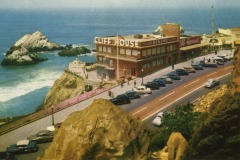 A vintage image of Cliff House in San Francisco, a two-story restaurant perched on a seaside cliff with parked cars along the road, overlooking the ocean and rugged rocky outcrops in the background.