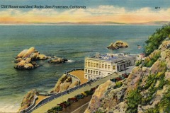 Vintage postcard showing the Cliff House in San Francisco perched above the ocean, with Seal Rocks in the water and cars parked along the scenic road beside this iconic building.