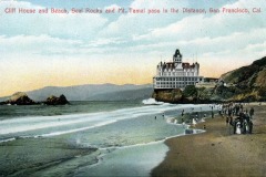 Vintage postcard showing San Francisco’s iconic Cliff House perched above a beach, with people strolling along the shore and Seal Rocks in the ocean; hills and distant mountains form the stunning backdrop.