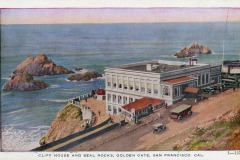 Vintage postcard of San Francisco’s iconic Cliff House, perched on a cliff above the Pacific Ocean, with Seal Rocks in the water and several early 20th-century cars parked nearby, capturing a classic coastal scene.