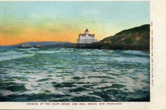 A historic illustration of Cliff House on San Francisco’s rocky shoreline at sunset, with waves in the foreground and Seal Rocks offshore. The orange and blue sky accentuates the scenic coastal landscape.
