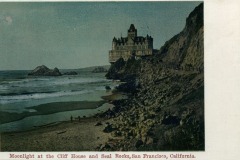 The historic Cliff House, perched atop a cliff in San Francisco, overlooks the ocean at sunset, with waves crashing below and Seal Rocks visible in the water.