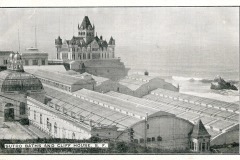 A vintage black-and-white photograph of the Sutro Baths and Cliff House in San Francisco, showing large glass-roofed buildings beside the ocean and a rocky shoreline in the background.