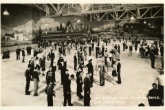 Vintage photo of a crowded indoor ice skating rink at Sutro Baths in San Francisco. People of all ages skate and gather on the ice, with a mural of alpine scenery and the historic Cliff House nearby.