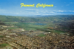 Aerial view of Fremont, California, showcasing a mix of residential areas and open green spaces under a clear blue sky. Rolling hills are visible in the background, with bold yellow text at the top reading Fremont, California.