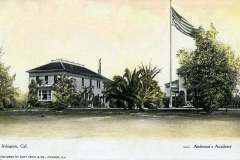 Vintage postcard of Andersons Academy in Irvington, California. It features two large buildings surrounded by trees, with an American flag on a tall flagpole in the garden.