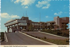 A vintage postcard shows Fremont, Californias City Hall and Civic Center. The building has a modern architectural design with wide steps leading up, surrounded by landscaping under a blue sky with scattered clouds.