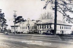 A vintage photograph of a building labeled Grammar School Centerville, Calif. The structure has a central entrance with steps, flanked by two symmetrical wings. Trees and a utility pole are visible, with a car parked on the street in front.