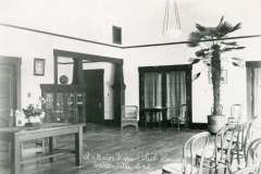 Black and white vintage photo of a club house interior in Centerville, California, with wooden chairs, potted plants, a large cabinet, and small tables. A handwritten label reads, Interior View Club House, Centerville.