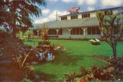 International Kitchen, Niles, California.  A scenic garden with a pond and flowers in the foreground. In the background, a large building with a sign reading International Kitchen sits under a partly cloudy sky. Trees and well-manicured grass complete the tranquil setting.