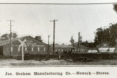 Black and white photo of industrial buildings with signs reading Jas. Graham Manufacturing Co. and Stoves, Ranges & Heaters. Power lines and trees are visible. The text below the image reads Jas. Graham Manufacturing Co.—Newark—Stoves.
