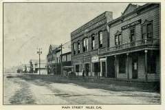 A black and white vintage photo of Main Street in Niles, California, featuring historic buildings. The Niles Hotel is prominently visible on the right. The street appears empty, and the architecture is reminiscent of the early 20th century.