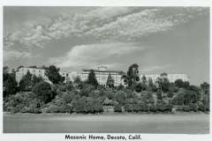 Black-and-white photo of Masonic Home in Decoto, California, set on a hill with a variety of trees in the foreground. The sky is partly cloudy.