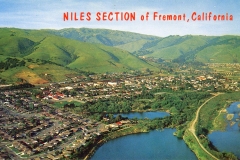 Aerial view of the Niles section in Fremont, California, showcasing a residential area with houses nestled against lush green hills. A body of water and a railway line are visible, with NILES SECTION of Fremont, California written across the top.