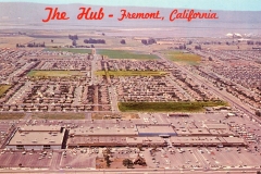 Aerial view of The Hub shopping center in Fremont, California, with large parking lots surrounding it. Residential neighborhoods and fields are visible in the background. Red text at the top reads The Hub - Fremont, California.