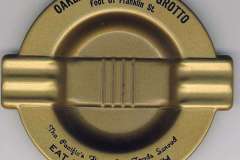 A gold-toned ashtray from the iconic Oakland Sea Food Grotto Restaurant in California features text: Foot Of Franklin St, The Pacifics Finest Sea Foods Served, and Eat Fish For Health. Its design includes raised ridges across the holding area.