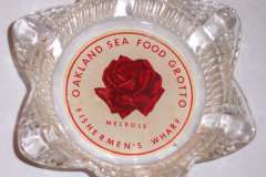 A star-shaped glass ashtray with a central label featuring a red rose. The text encircling the rose reads, Jack London Squares Grotto Restaurant and Fishermens Wharf Melrose.