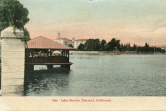 Vintage postcard depicting Lake Merritt in Oakland, California. It features a gazebo-like structure over the water, surrounded by lush greenery, with buildings in the background under a pink and blue sky.