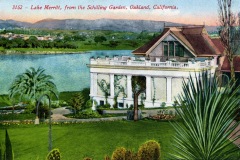 A historic postcard image of a grand house overlooking Lake Merritt in Oakland, California. The building is surrounded by lush greenery, palm trees, and vibrant gardens against a backdrop of distant hills and a pastel-colored sky.