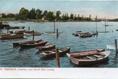 A vintage postcard shows boats docked at Lake Merritt Boat Landing in Oakland, California. The lake is calm, surrounded by trees and small buildings in the background.
