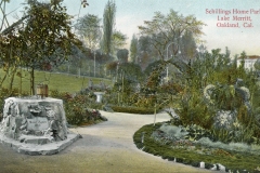 A vintage postcard depicts Schillings Home Park in Lake Merritt, Oakland, California. The scene features a landscaped garden with winding paths, lush greenery, a stone fountain with a basin, and distant trees under a serene sky.