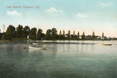 A vintage postcard of Lake Merritt in Oakland, California, featuring calm water with small boats. The shoreline is lined with trees and houses, under a partly cloudy sky.