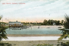 A vintage postcard image of Lake Merritt in Oakland, California. It features a serene body of water with small boats and a house on stilts. Trees line the background beneath a soft blue and pink sky. Palm leaves frame the foreground.