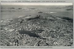 Aerial black and white photo of the Oakland area in California, featuring Lake Merritt in the foreground. The San Francisco-Oakland Bay Bridge and Golden Gate Bridge are visible in the background. Dense urban landscape with roads and buildings.