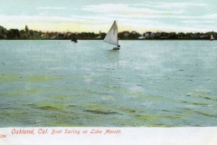 Vintage postcard depicting sailboats on Lake Merritt in Oakland, California, with a tranquil water surface reflecting the sky. A sailboat prominently glides across the lake against a backdrop of trees and a distant shoreline.