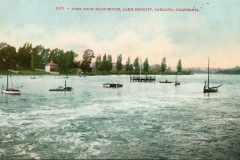A vintage postcard shows a view of Lake Merritt, Oakland, California, from a boathouse. Small sailboats float on the water, with trees and a few buildings visible on the shore in the background. The caption reads, 1679 - View from boat-house.