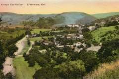 A scenic view of Arroyo Sanitarium in Livermore, California, nestled among green hills. The facility is surrounded by lush vegetation and winding roads. Bright, clear sky enhances the tranquil setting.