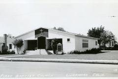Black and white photo of First Baptist Church in Livermore, California. The church has a gabled roof with a cross above the entrance. A signboard is near the front steps. Trees and a house are visible in the background.