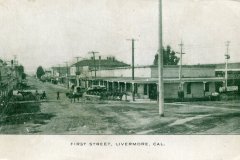 A vintage photo of First Street in Livermore, California, showing a dirt road with horse-drawn carriages, wooden buildings, and utility poles lining the street, capturing an early 20th-century small-town scene.