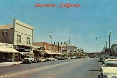 Looking East on South First Street. A vintage postcard showcasing a busy street in Livermore, California. The scene features parked classic cars on both sides of the road, shops with distinctive 1960s signage, and Livermore, California written across the top in red .
