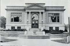 Black and white photo of a historic building labeled Public Library, Livermore. The structure features a central entrance with columns, large windows, and a decorative pediment. A round fountain sits in the foreground, surrounded by a lawn.