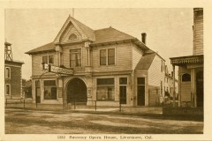 Sepia-toned vintage photograph of Sweeney Opera House, an old wooden building with a symmetrical facade, arched windows, and a central triangular pediment. Located in Livermore, California, with a sign above the entrance and neighboring structures visible.