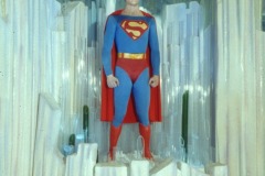 Christopher Reeve as Superman at Movieland Wax Museum stands confidently inside a crystal-like structure, resembling the Fortress of Solitude, surrounded by tall, translucent pillars in his classic red and blue costume.