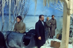 Four people in winter coats stand beside a black sleigh and luggage in a snowy, icy landscape at Movieland. The somber, staged setting features Dr. Zhivago wax figures amid frost-covered trees and icicles.