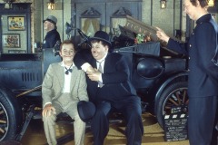 Two wax figures of Laurel and Hardy at Movieland Wax Museum sit in front of a vintage car—one with an ice cream cone—while a third, dressed as a policeman, holds a ticket sign in the vintage-style room.