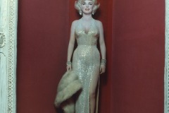 A Marilyn Monroe wax figure at Movieland Wax Museum stands in a red alcove, wearing a sparkling, floor-length silver gown with a high slit, holding a fur stole and smiling, with glamorous makeup and jewelry.