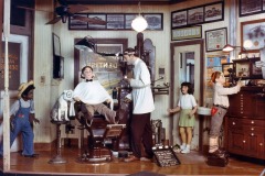 Our Gang figures at Movieland Wax Museum features a vintage dentist office scene. A dentist with a young patient in the chair, is watched by a dog and three other children. The room has old-fashioned decor, dental equipment, certificates, and photos on the walls.