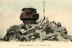 Historic image of the Marine Observatory, a wooden octagonal structure, atop rocky terrain on Mt. Tamalpais, California. Several people stand on the rocks and observatory balcony. A tall weather instrument is visible nearby.