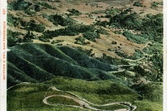 A vintage postcard showing a panoramic view from Mt. Tamalpais in San Francisco, featuring winding mountain roads and expansive landscapes. In the distance, the San Francisco Bay, Alcatraz, and Angel Island are visible. Text details landmarks.