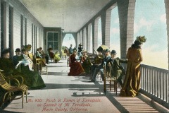 Illustration of people in period clothing relaxing on the porch of the Tavern of Tamalpais, Mount Tamalpais, California. The porch is lined with chairs and some attendees are seated while others stand, all facing the scenic view.