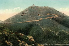 Vintage postcard of Mount Tamalpais summit in California, with a winding path leading up to a small building and tower at the peak. The foreground features green vegetation and colorful wildflowers.