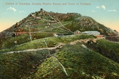 Vintage postcard of Mount Tamalpais summit, featuring a network of winding paths leading to structures labeled as the Weather Bureau and Tavern of Tamalpais. The landscape is lush and green under a clear blue sky.