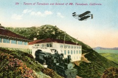 A vintage postcard depicts a train approaching the Tavern of Tamalpais on a mountain, with a historic airplane flying overhead. Rolling hills and a clear sky enhance the scenic setting. Text reads: 384 - Tavern of Tamalpais and Summit of Mt. Tamalpais, California.